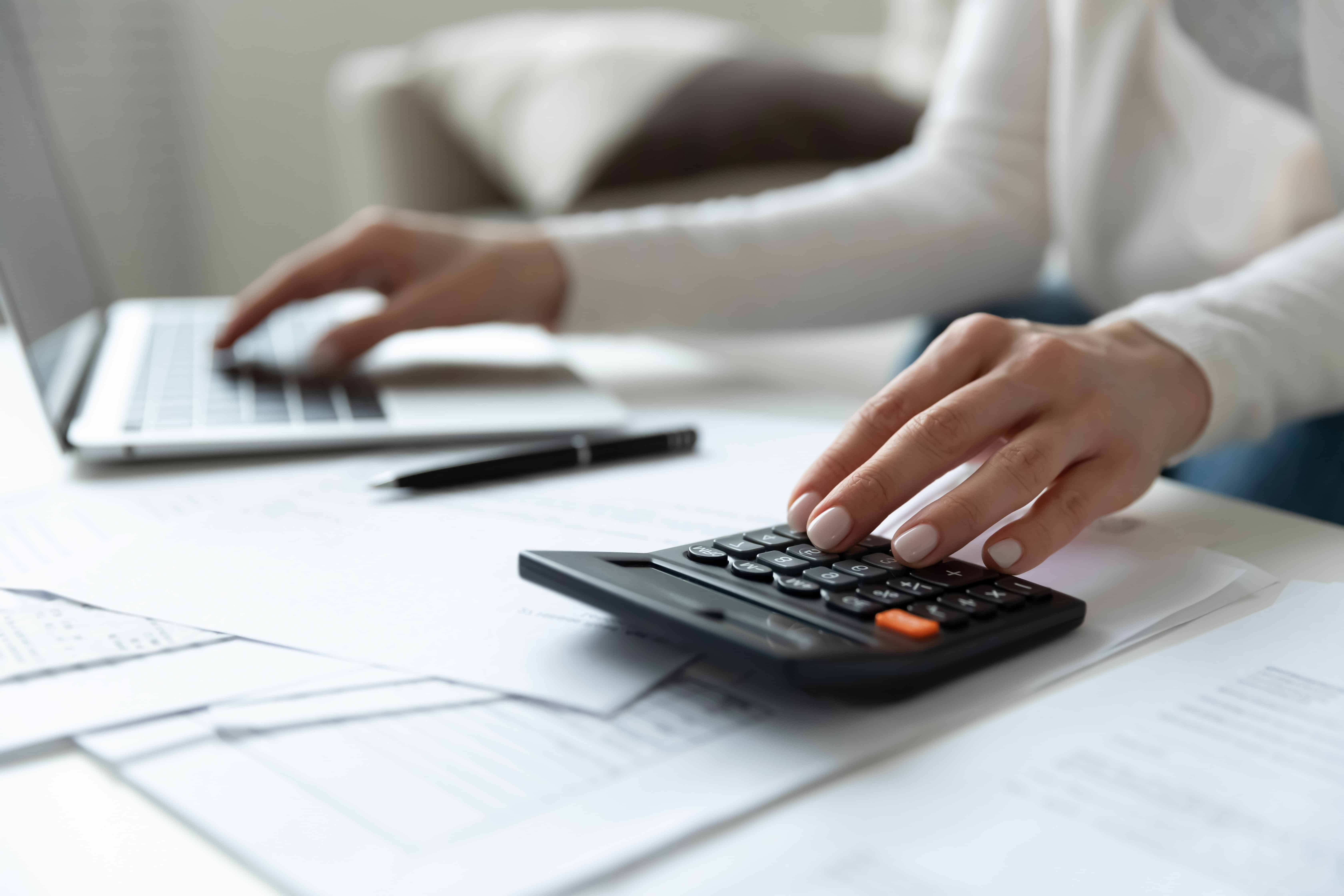 Close up of a woman using a laptop and a calculator